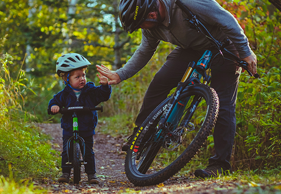 an adult high fiving a young kid while on a bike trail with their bikes